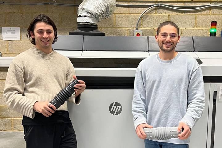 Two men standing next to a machineDescription automatically generated